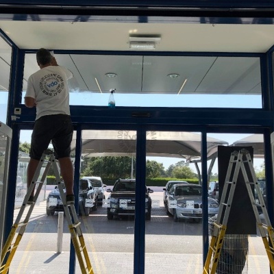 Homem em escada a trabalhar em porta automática de vidro azul em entrada de loja