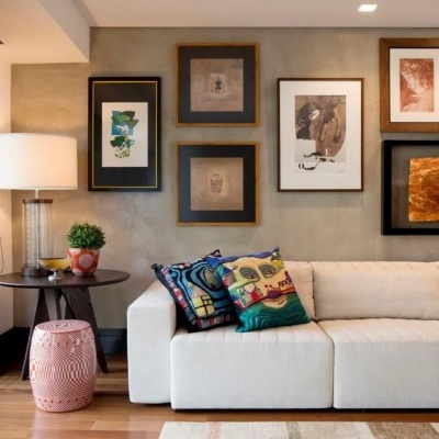 Sala de estar com sofá branco, almofadas coloridas, mesa de madeira, candeeiro e quadros na parede