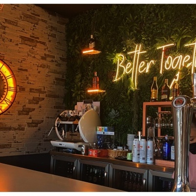 Interior de bar com relógio grande iluminado e letreiro néon 'Better Together'