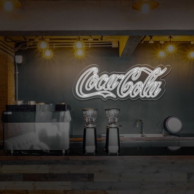 Mostrador de bar com máquinas de café e logo Coca-Cola iluminado na parede preta