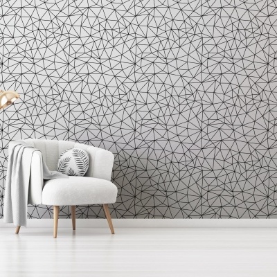 Poltrona cinza clara com almofada decorativa em ambiente minimalista com candeeiro de pé dourado e parede com papel de parede geométrico.