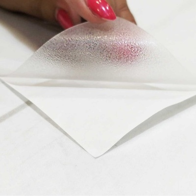 Folha transparente texturizada sendo segurada por mão com unhas vermelhas