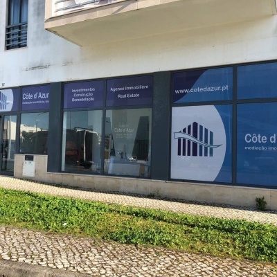 Fachada de agência imobiliária com vinis azuis e brancos com textos em francês e português