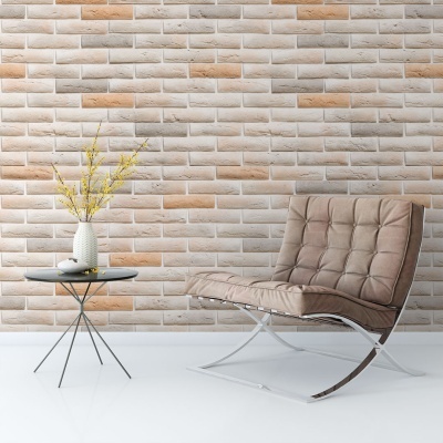 Cadeira castanha clara com pernas metálicas e mesa preta com vaso branco e flores amarelas junto a parede de tijolos claros.