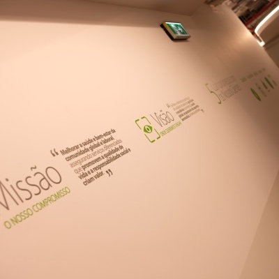 Parede branca com textos em português sobre missão e visão, decorada com ícones verdes em corredor iluminado