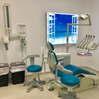 Cadeira dentária azul em consultório com equipamentos e painel luminoso de praia na parede