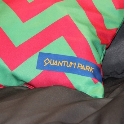 Almofada vermelha e verde com etiqueta QUANTUM PARK sobre tecido preto