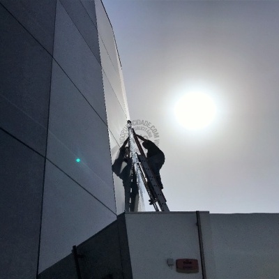 Trabalhador na escada junto a parede exterior sob sol forte