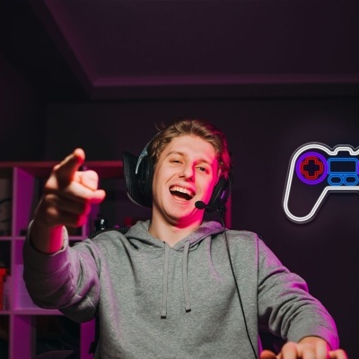 Jovem com comando de videojogos e auscultadores num quarto iluminado a roxo