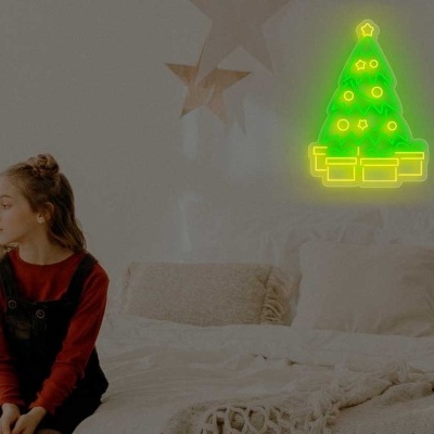 Luz de néon em forma de árvore de Natal verde numa parede branca ao lado de cama com menina sentada