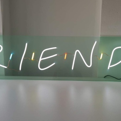Placa de luz verde com texto 'FRIENDS' iluminado em branco com pontos laranja