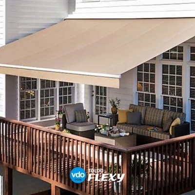 Toldo beige instalado numa varanda de madeira com mobiliário de exterior e janelas brancas.