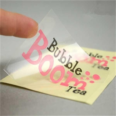 Etiqueta transparente com texto Bubble Boom Tea em rosa e preto, segurada por um dedo