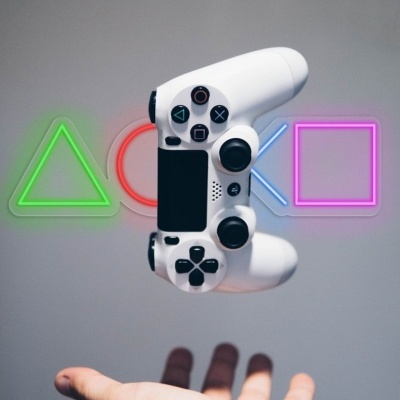 Comando de jogo PlayStation branco com botões pretos e símbolos neon ao fundo