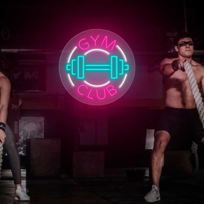 Duas pessoas a usar cordas de treino numa academia com sinal neon 'GYM CLUB'