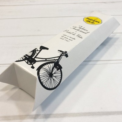 Embalagem branca triangular com ilustração preta de bicicleta e texto sobre madeira branca.