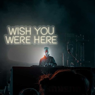 Pessoa num concerto com letreiro luminoso 'WISH YOU WERE HERE' ao fundo