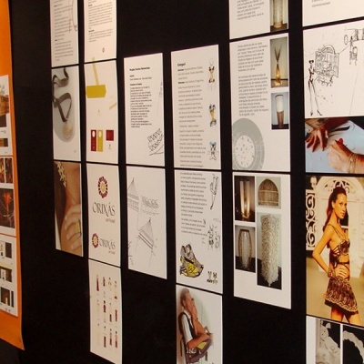 Painéis verticais com documentos e imagens de design expostos numa parede preta.