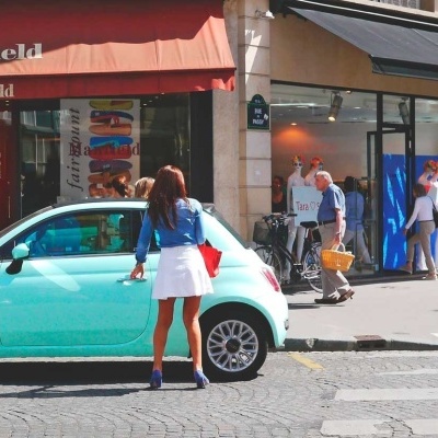 Carro verde-água estacionado junto a loja com letreiro 'BLACK FRIDAY' e mulher em pé ao lado