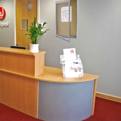 Receção de escritório com secretária em madeira clara e planta verde