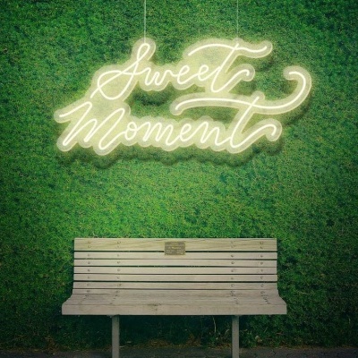 Banco branco de madeira em frente a parede verde com letreiro luminoso 'Sweet Moment'