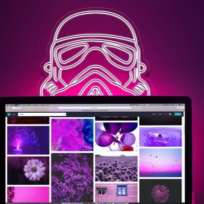 Monitor com imagens em roxo, luz néon rosa em forma de capacete Stormtrooper, smartphone ao lado.