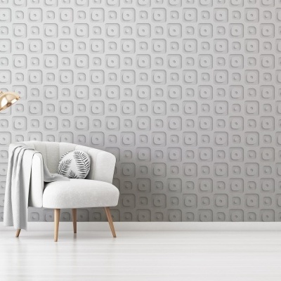 Poltrona branca com almofada decorativa e manta cinzenta acompanhada por candeeiro dourado, frente à parede cinzenta com padrão geométrico