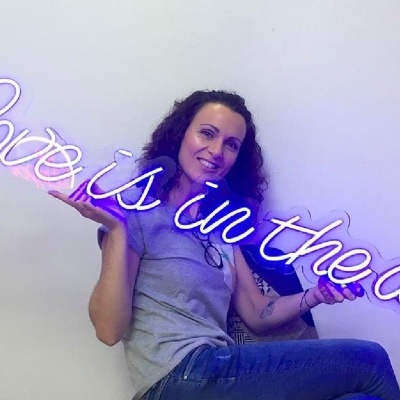 Letreiro luminoso neon lilás 'Love is in the air' segurado por mulher