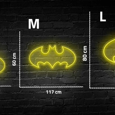 Letreiros de néon amarelo do símbolo do Batman em três tamanhos, montados numa parede de tijolos preta.