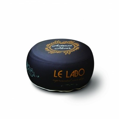 Pufe redondo preto com texto dourado LE LABO e ornamentos no topo.