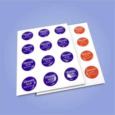 Adesivos redondos brilhantes roxos e laranja com texto QinetiQ V.I.P Day 6 Guest em folhas brancas