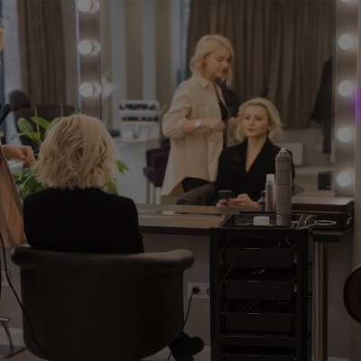 Salão de cabeleireiro com profissional a alisar cabelo de cliente e espelhos iluminados