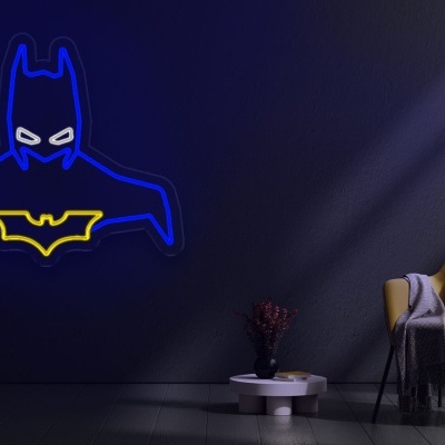 Decoração em neon do Batman azul e amarelo numa parede cinza, ao lado de cadeira amarela e planta