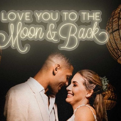 Casal sorrindo sob luminárias trançadas e texto luminoso 'LOVE YOU TO THE Moon & Back' ao fundo