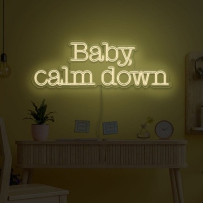 Letreiro de néon com texto 'Baby calm down' numa parede amarela