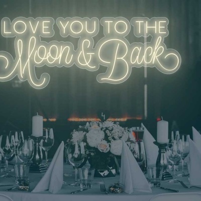 Mesa de jantar elegante com letreiro luminoso LOVE YOU TO THE Moon & Back ao fundo