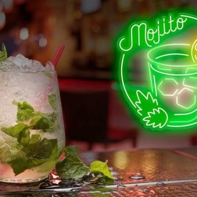 Copo de mojito com gelo e hortelã num bar com letreiro de néon verde a dizer Mojito