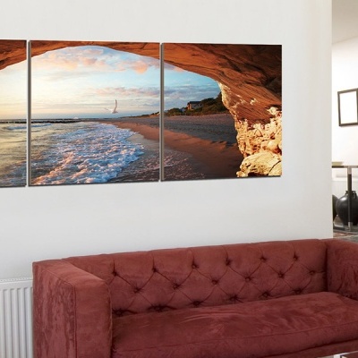 Conjunto de três quadros com paisagem de praia pendurados sobre sofá vermelho em interior