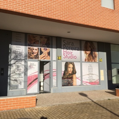 Fachada de um salão de cabeleireiro com imagens de mulheres e texto promocional