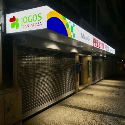 Fachada de loja com placa iluminada e portas metálicas fechadas à noite