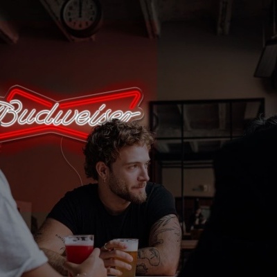 Interior de bar com pessoas e letreiro luminoso Budweiser