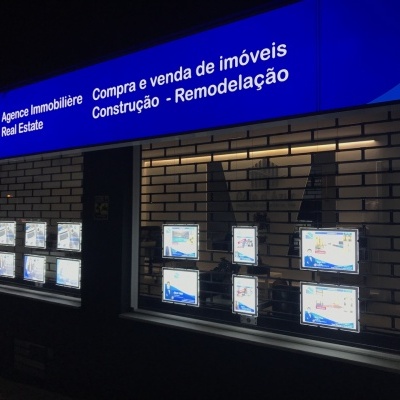Fachada iluminada de imobiliária com anúncios de imóveis e letreiro azul