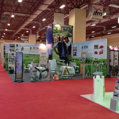 Stand de feira com decoração verde e branco da marca TETA, mesas, cadeiras e painéis de agricultura