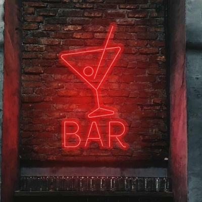 Placa de néon vermelha 'BAR' com desenho de copo de cocktail numa parede de tijolos