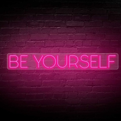 Sinal de néon rosa 'BE YOURSELF' numa parede de tijolos escura