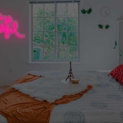 Quarto com cama arrumada, almofadas coloridas, janela e luz neon rosa na parede