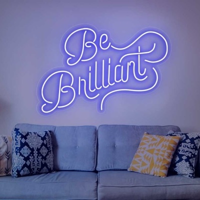 Sofá cinzento claro com almofadas coloridas e placa de néon azul 'Be Brilliant' na parede