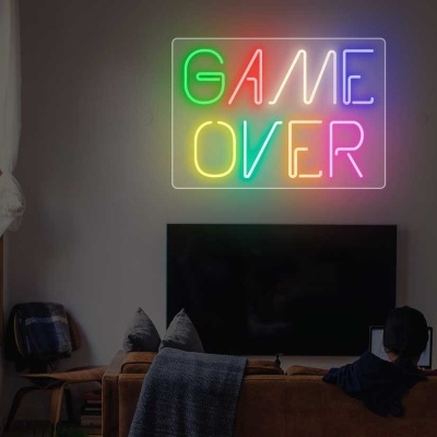 Letreiro de néon colorido com 'GAME OVER' numa sala com sofá e televisão