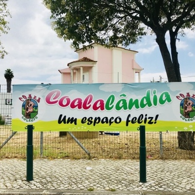 Banner colorido do Coala Colégio em espaço exterior com árvores e casa ao fundo