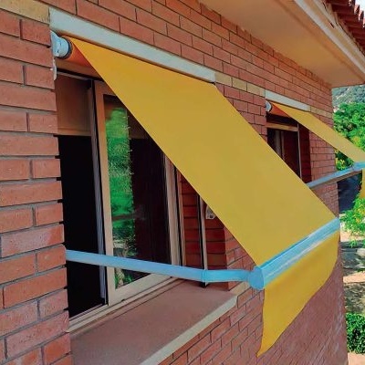 Três janelas com toldos amarelos numa parede de tijolos vermelhos com árvores e montanhas ao fundo